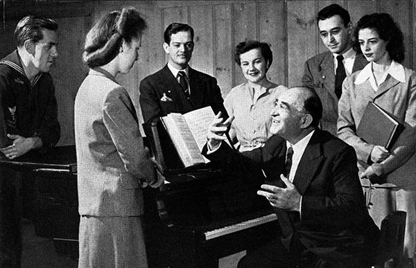 man at piano speaking with voice students